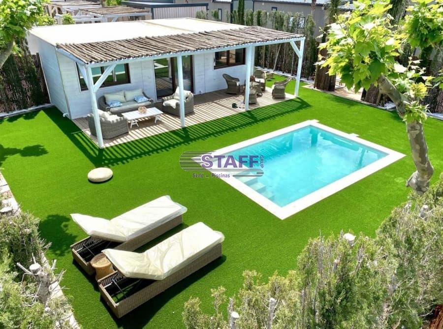 Small pool in a garden with grass, equipped with loungers and a wooden pergola creating a cozy outdoor space.